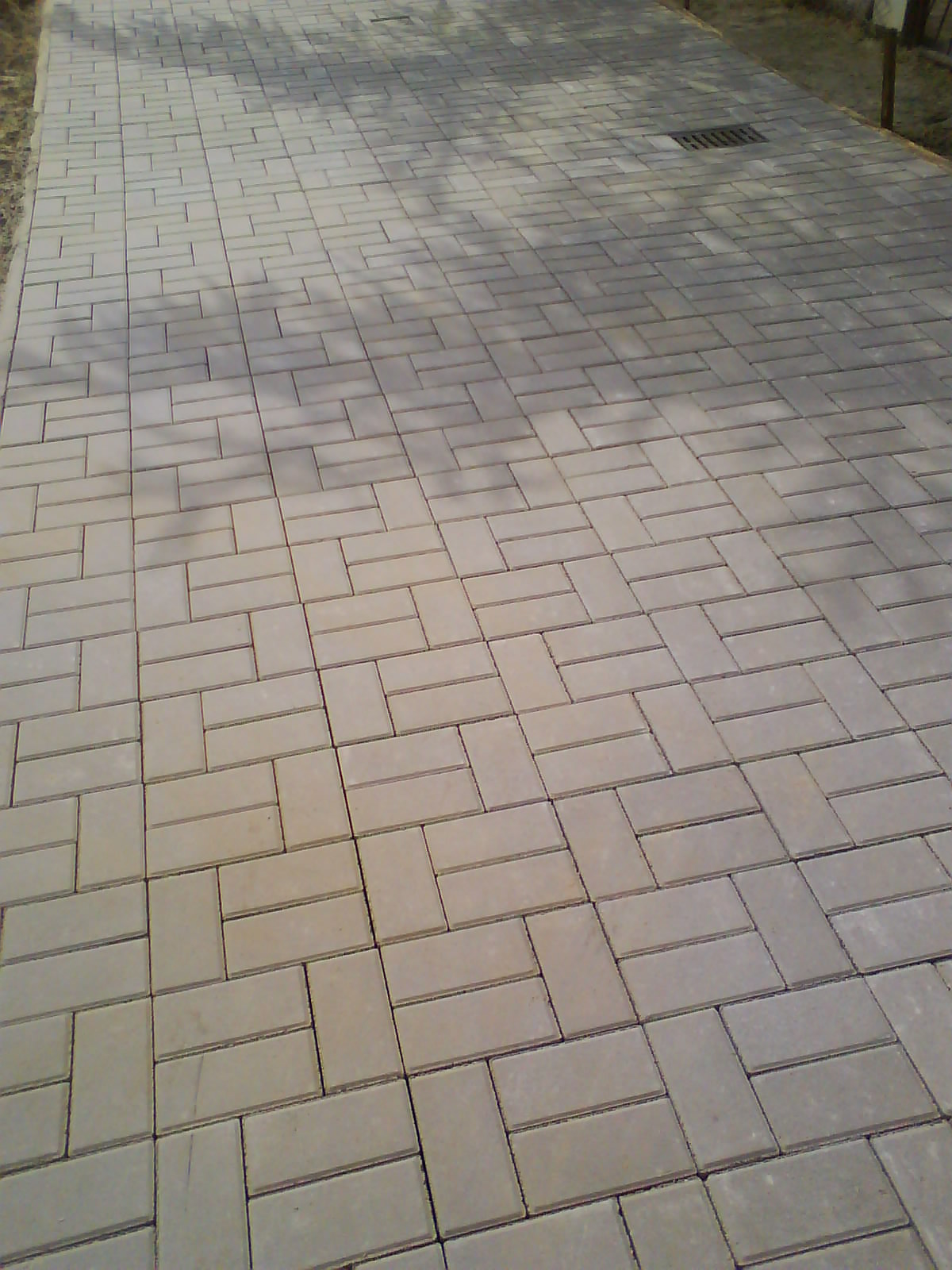 Ułożona szara kostka brukowa w jodełkę, widoczna studzienka kanalizacyjna, realizacja brukarska w Elblągu.